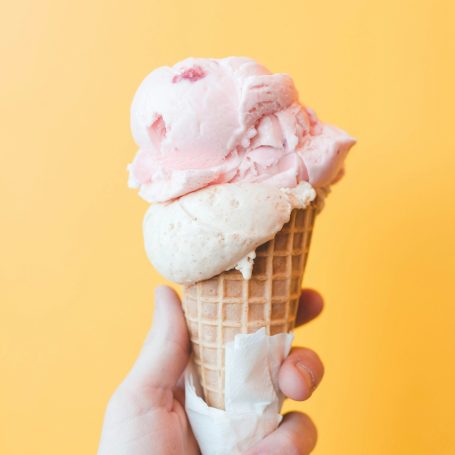 Eine Hand hält ein großes Eis in der Waffel, es könnte Erdbeer- und Vanilleeis sein